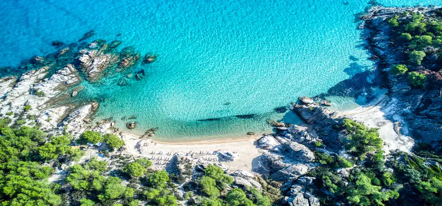 Vedere aeriană peste golful Portokali cu ape cristaline și coaste cu pini, Halkidiki Grecia - oferte hoteluri
